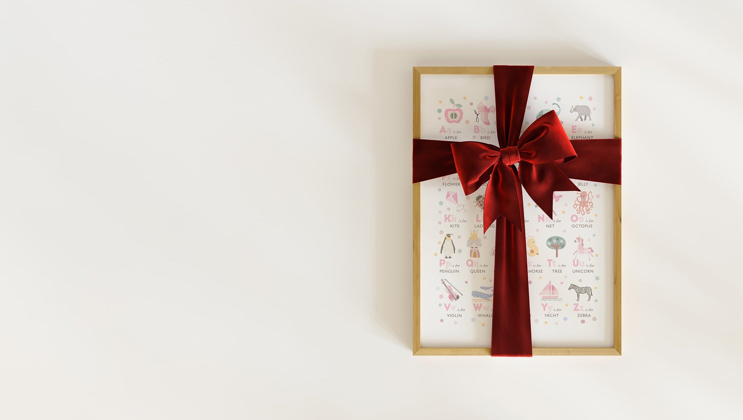 A framed educational girls alphabet art print, wrapped in a red velvet ribbon, representing an instant digital download gift.