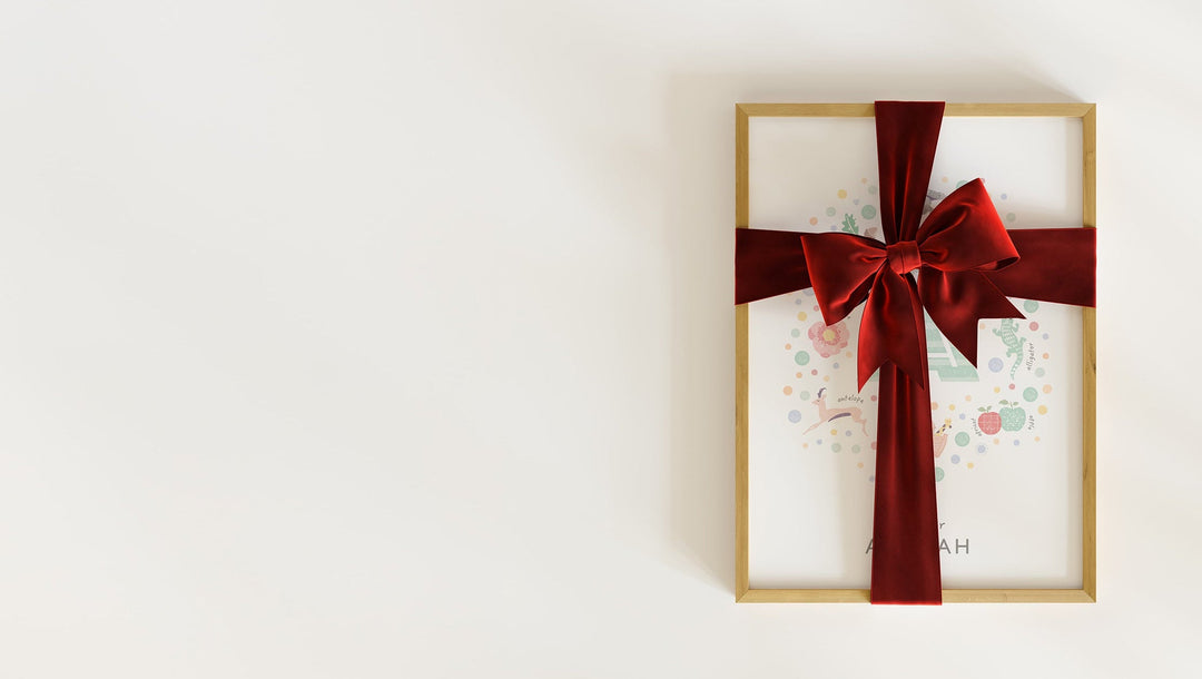 A framed, pastel-coloured personalised initial letter a print for a nursery, wrapped in a festive red velvet ribbon.
