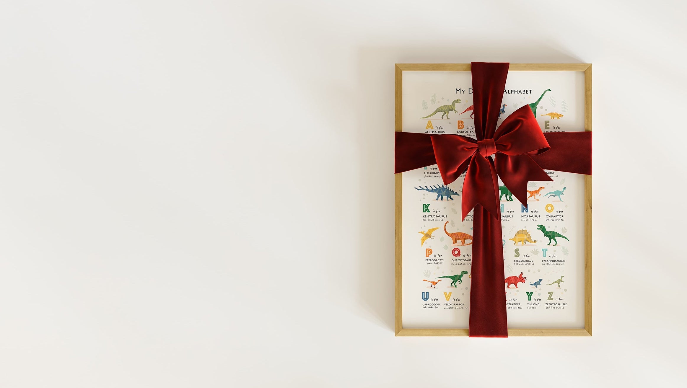 A framed illustrated dinosaur alphabet print wrapped in a red velvet ribbon,