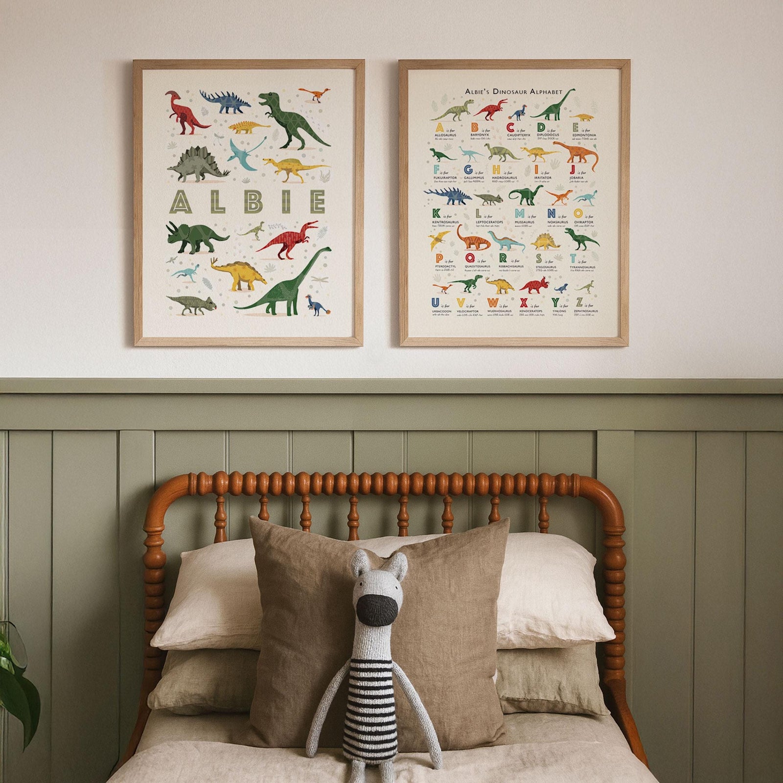 Set of two personalised dinosaur alphabet prints framed above a rustic children’s bed, with neutral tones and classic nursery styling.