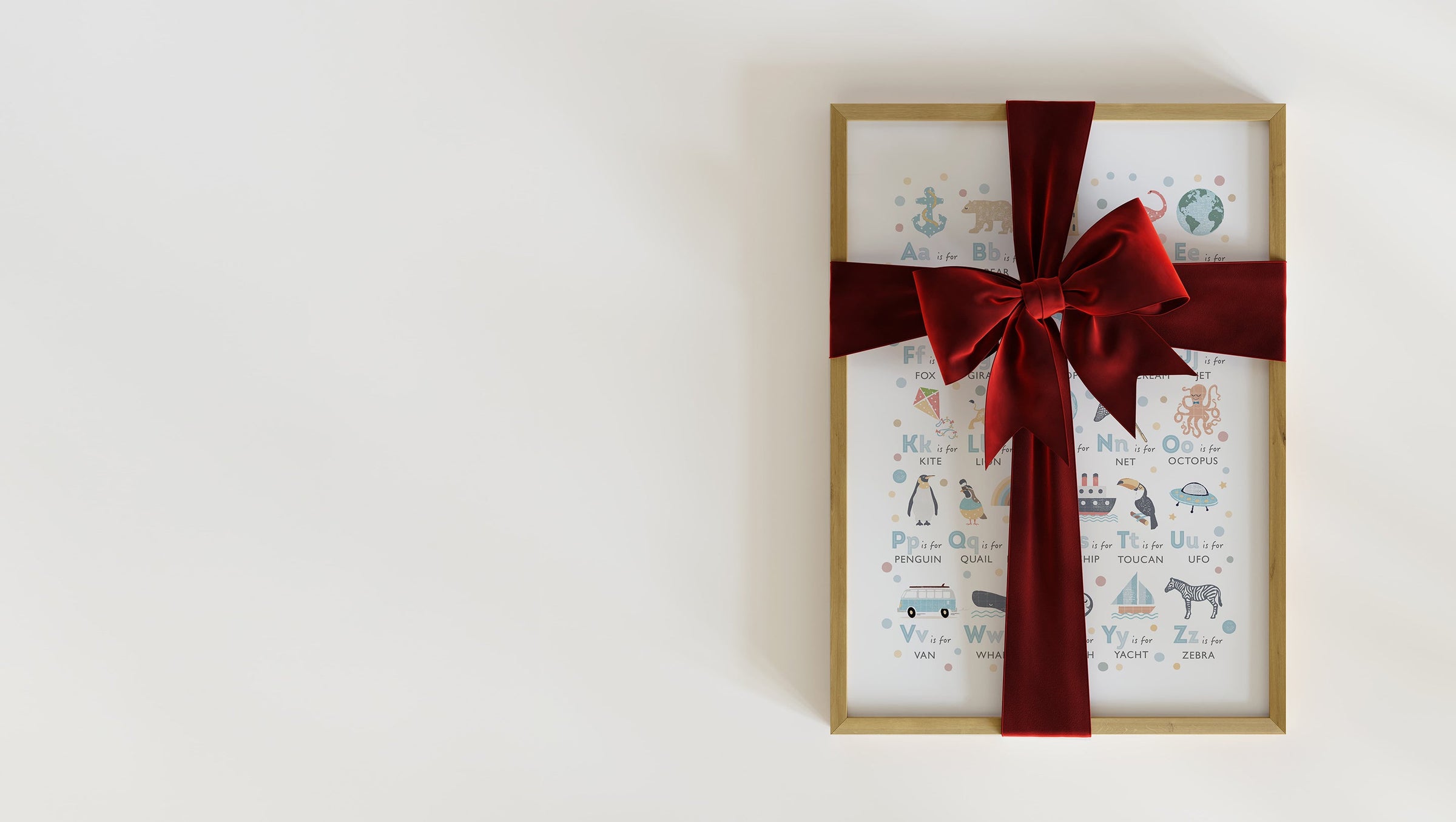 A beautiful, alphabet print in a frame, wrapped in a festive red ribbon, representing a perfect keepsake gift for a baby's first Christmas.
