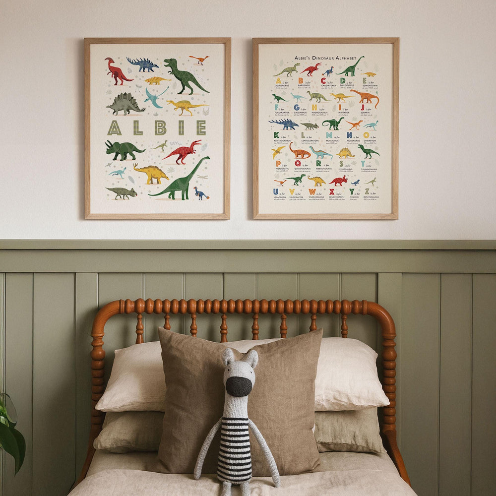 Set of two personalised dinosaur alphabet prints framed above a rustic children’s bed, with neutral tones and classic nursery styling.