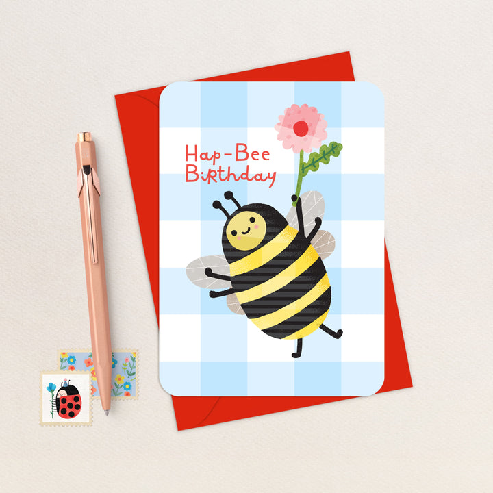 Birthday card with a bee design and red envelope on a light background