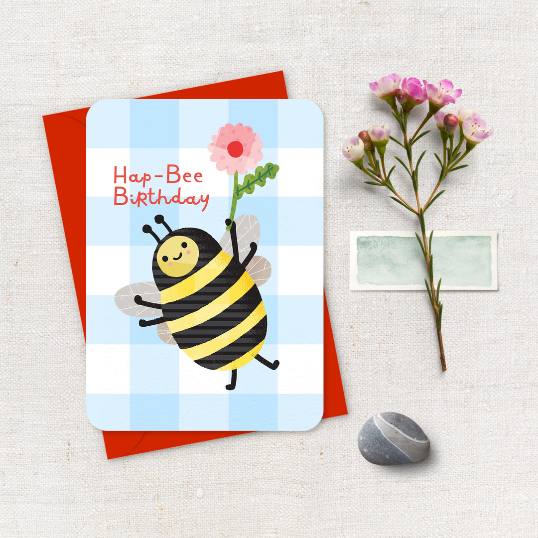 Birthday card with a bee design and red envelope on a textured surface.