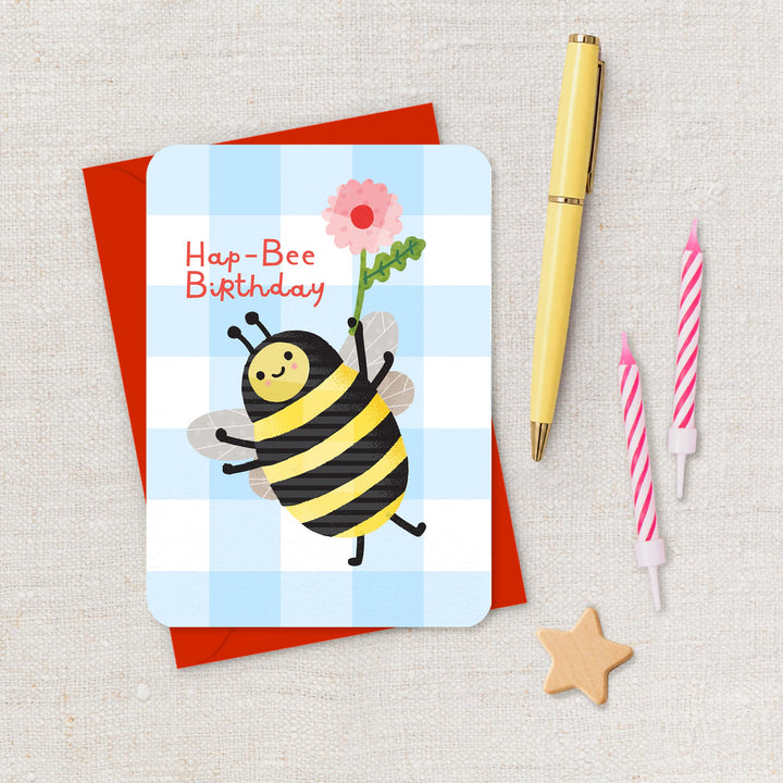 Birthday card with a bee design, pen, and candles on a textured surface