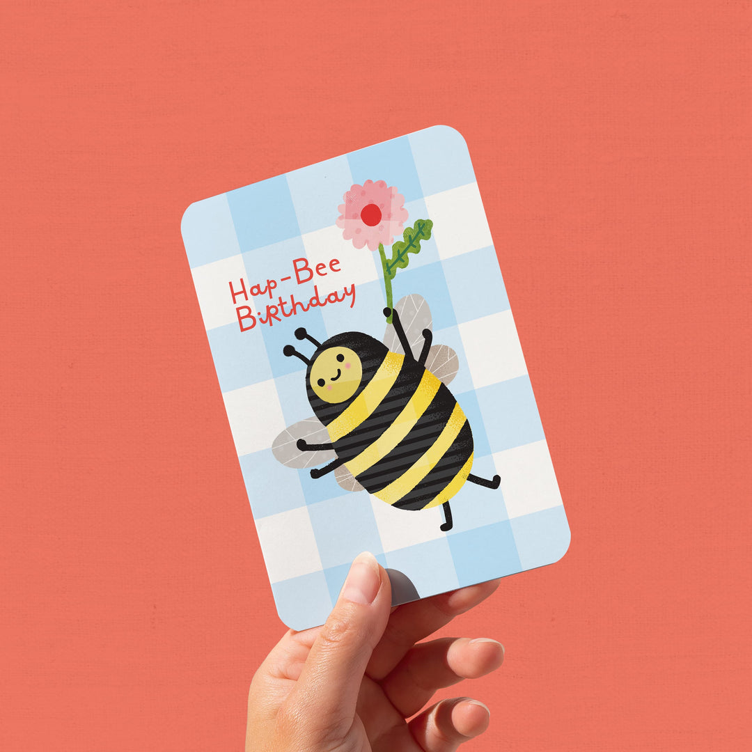 Hand holding a birthday card with a bee illustration and &