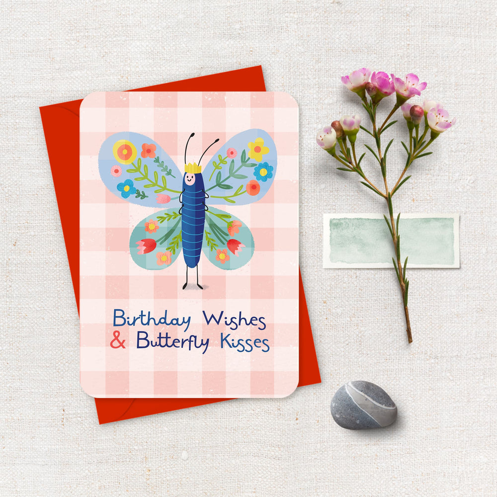 Greeting card with butterfly design and birthday wishes text, placed on a textured surface with flowers and a stone.