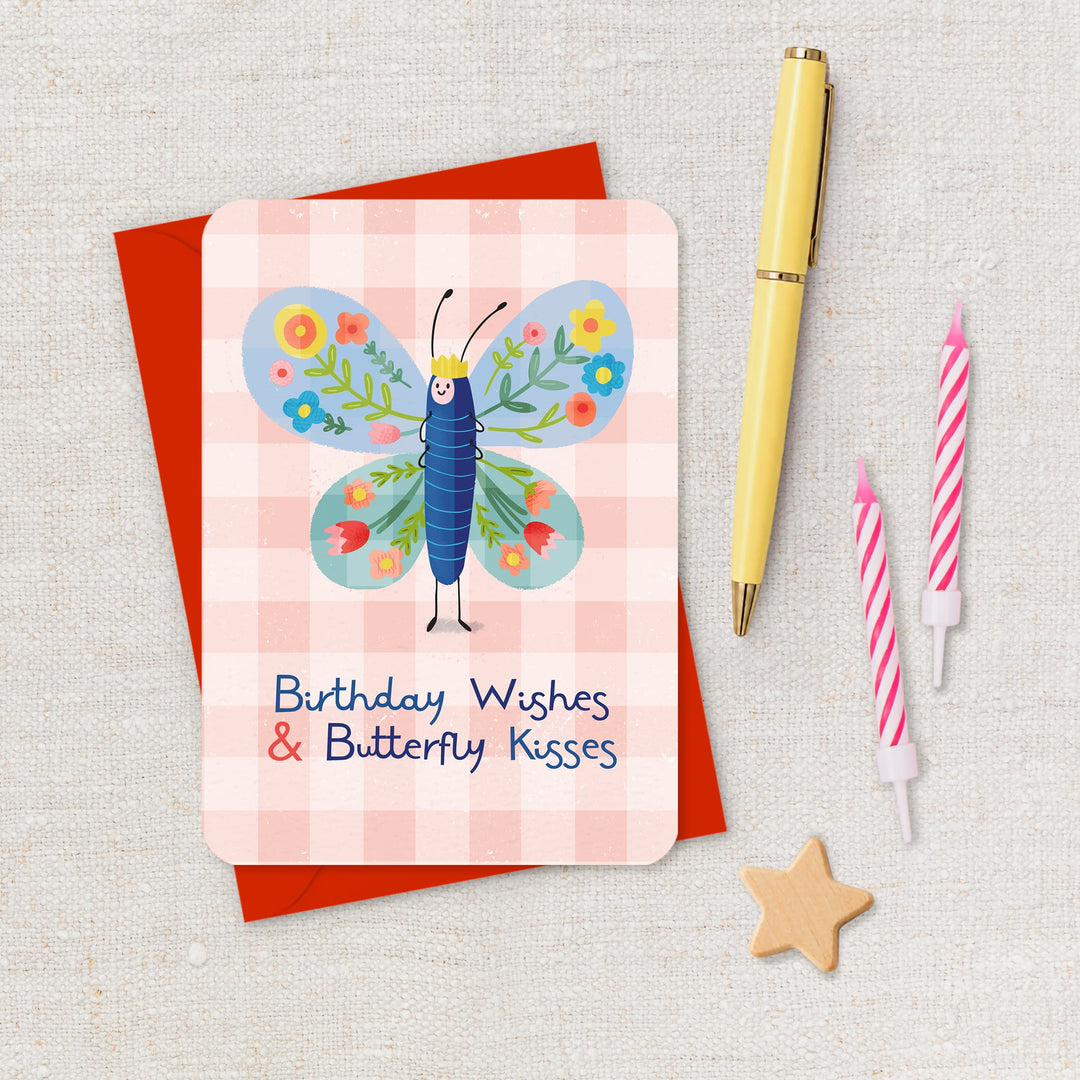 Greeting card with butterfly design and birthday wishes text, placed on a textured surface with a pen and candles.