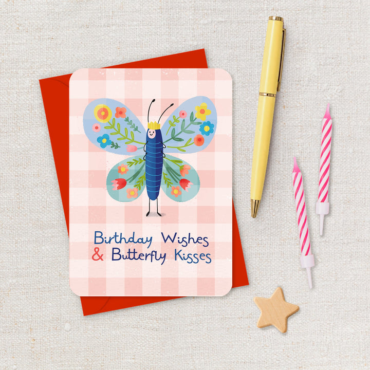 Greeting card with butterfly design and birthday wishes text, placed on a textured surface with a pen and candles.