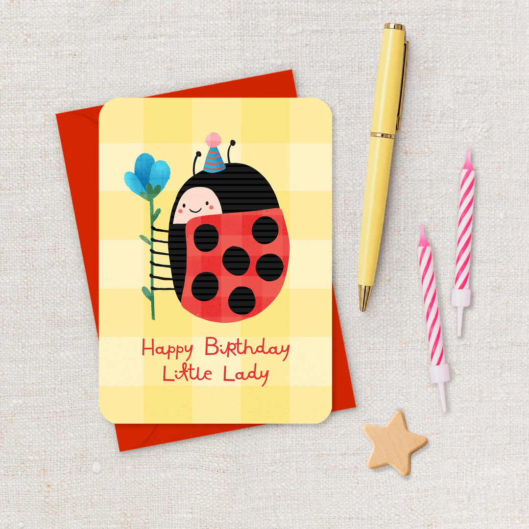 Birthday card with a ladybug design, pen, and candles on a textured surface