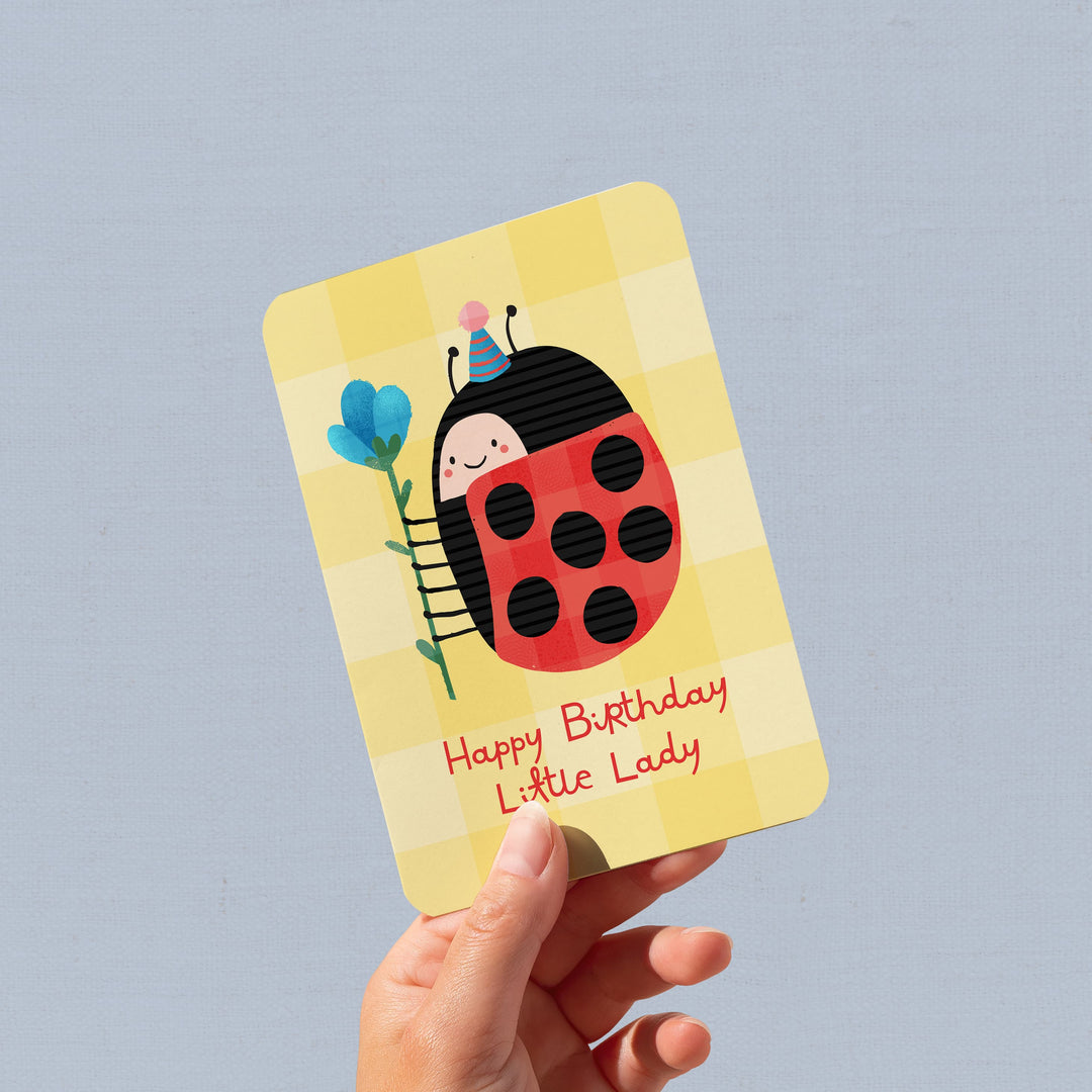 Hand holding a birthday card with a ladybug design on a gray background