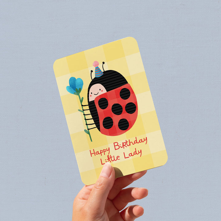 Hand holding a birthday card with a ladybug design on a gray background