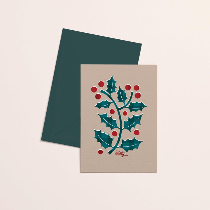 christmas card featuring abstract holly design on neutral background on top of dark green envelope