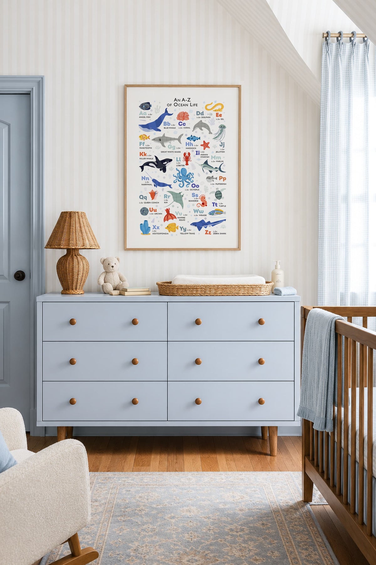 A framed educational 'Alula to Diving' sea life poster hangs on a wall above a light blue dresser in a styled nursery room.