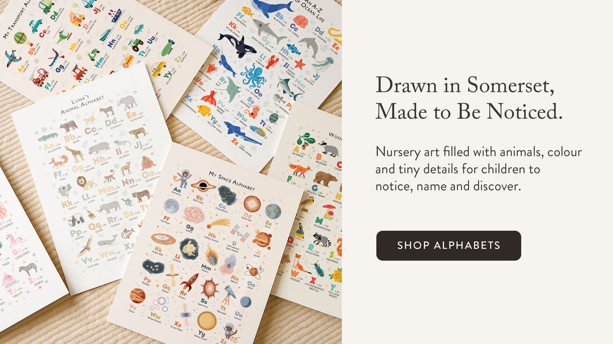 A set of children's nursery alphabet art prints featuring colourful animals, ocean creatures, transportation, and space illustrations arranged on a light rug surface next to a cream-colored text panel with promotional copy and a 'SHOP ALPHABETS' button.