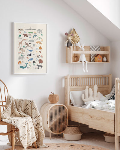 A cozy bohemian-style children’s room featuring a framed Animal Alphabet print on the wall above a natural wooden crib, complemented by soft toys and warm, textured decor items.