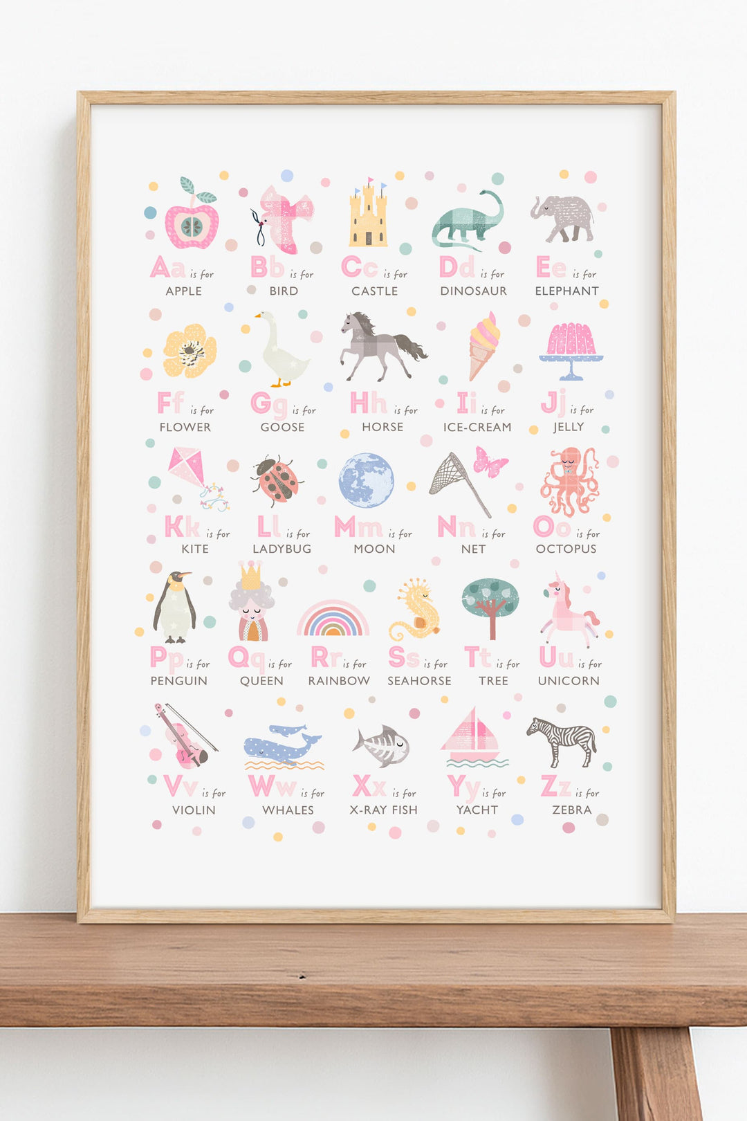 Framed pink alphabet poster with colourful illustrations on a wooden shelf in a kids room
