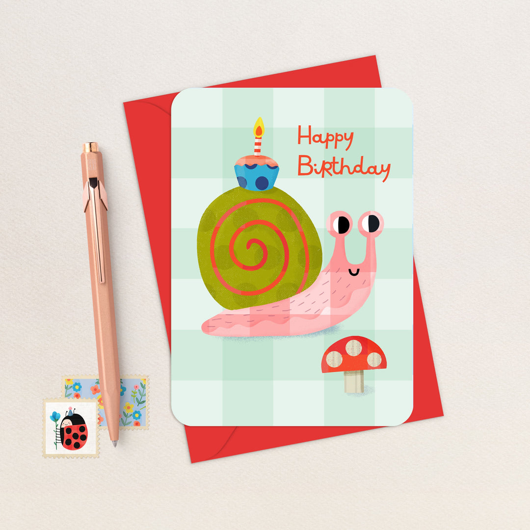 Birthday card with a snail illustration, pen, and stamp on a light background