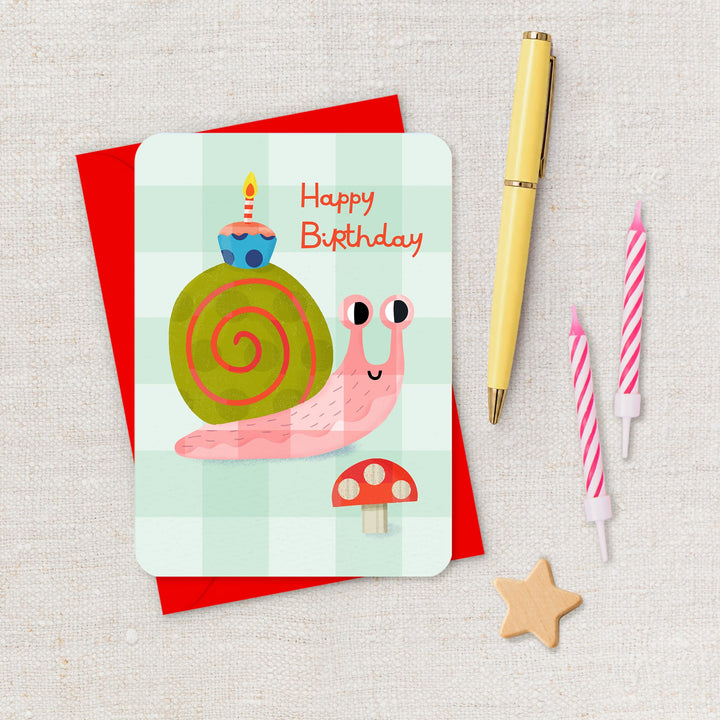 Birthday card with a snail illustration, candles, and a pen on a textured surface