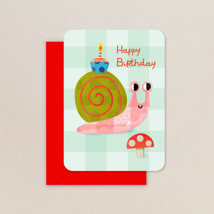 Birthday card with a pink snail, green shell, and cupcake with a candle on a light green background.