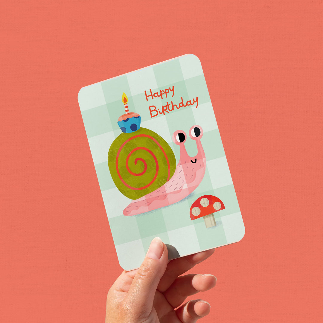 Hand holding a birthday card with a cartoon snail on a pink background