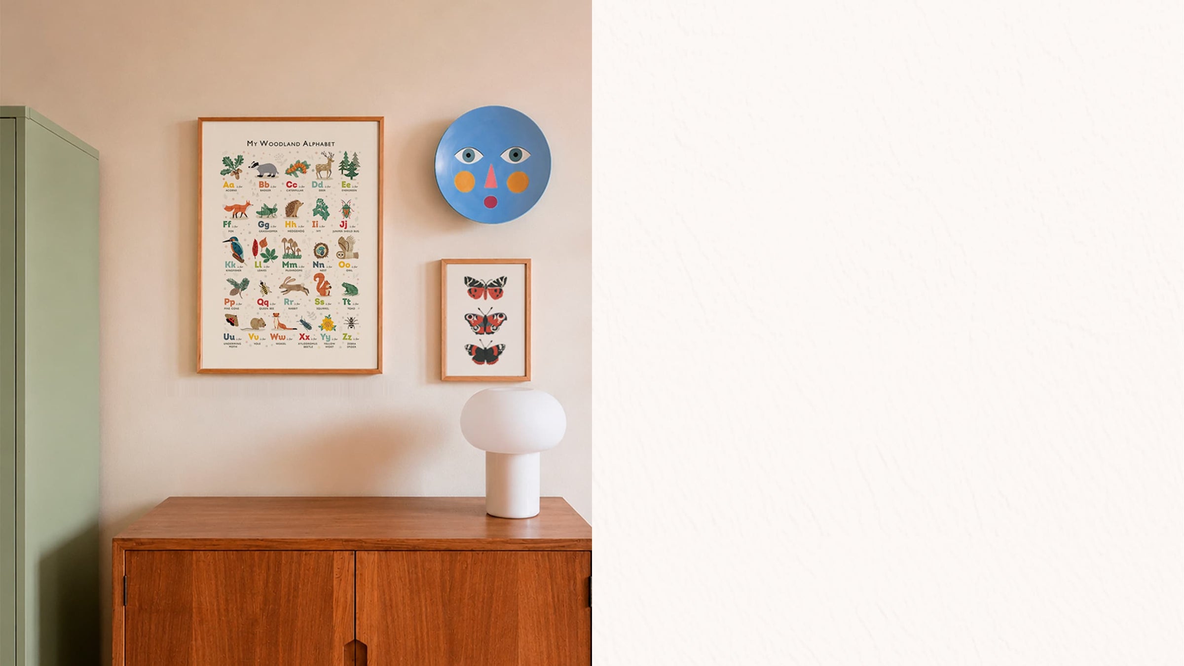 A styled interior scene showing framed wall art and decor hanging above a wooden cabinet. Visible items include a large framed educational animal print, a smaller framed butterfly print, a round blue plate-style wall decor piece, and a white table lamp.