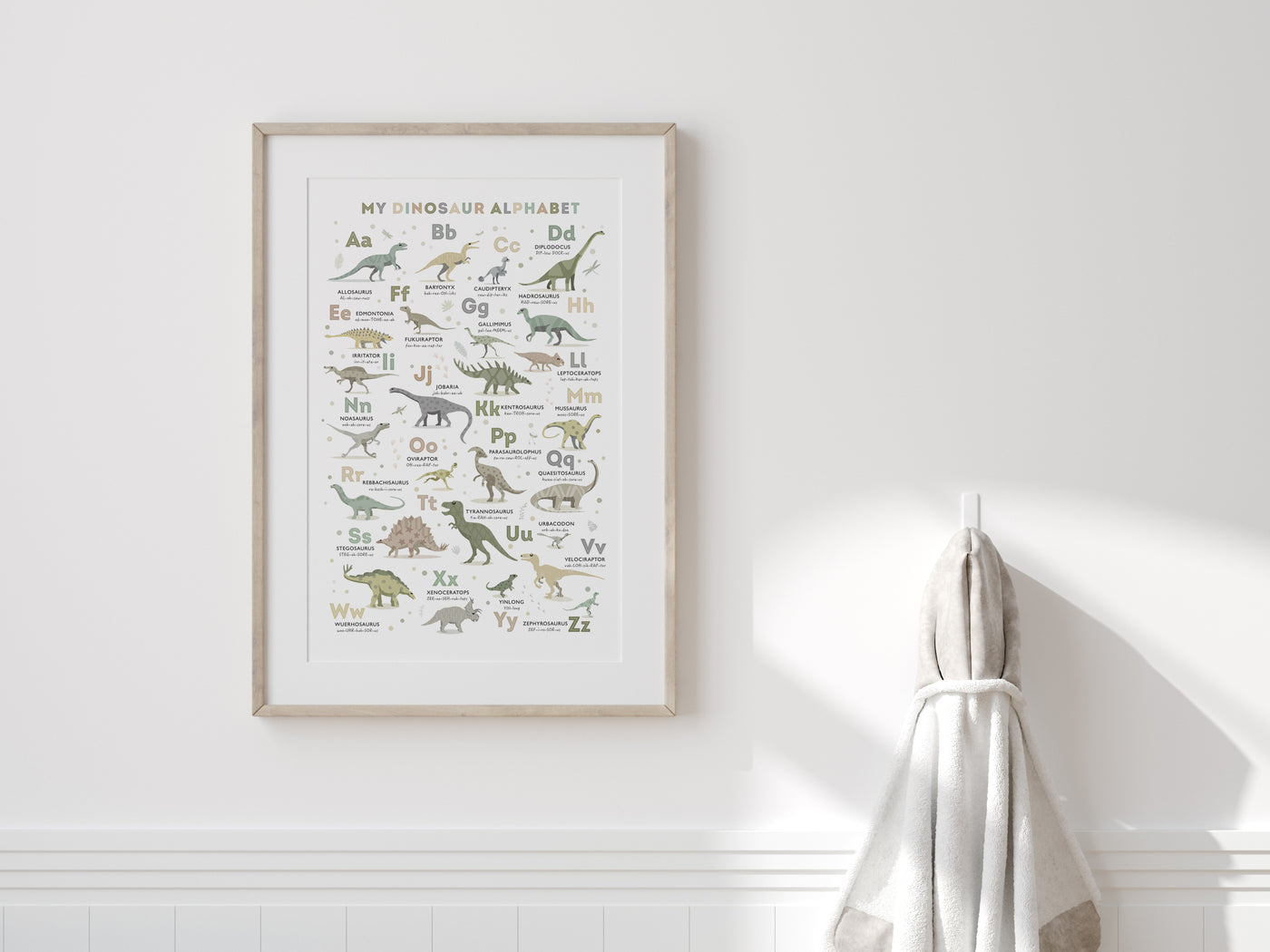 Dinosaur Alphabet Poster in Earth Tone Colours framed on a white wall with a neutral dressgown hanging next to it