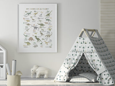 playroom scene with a framed version of the Dinosaur Alphabet Poster in Earth Tone Colours on a white wall with a play tent and toys in the foreground.