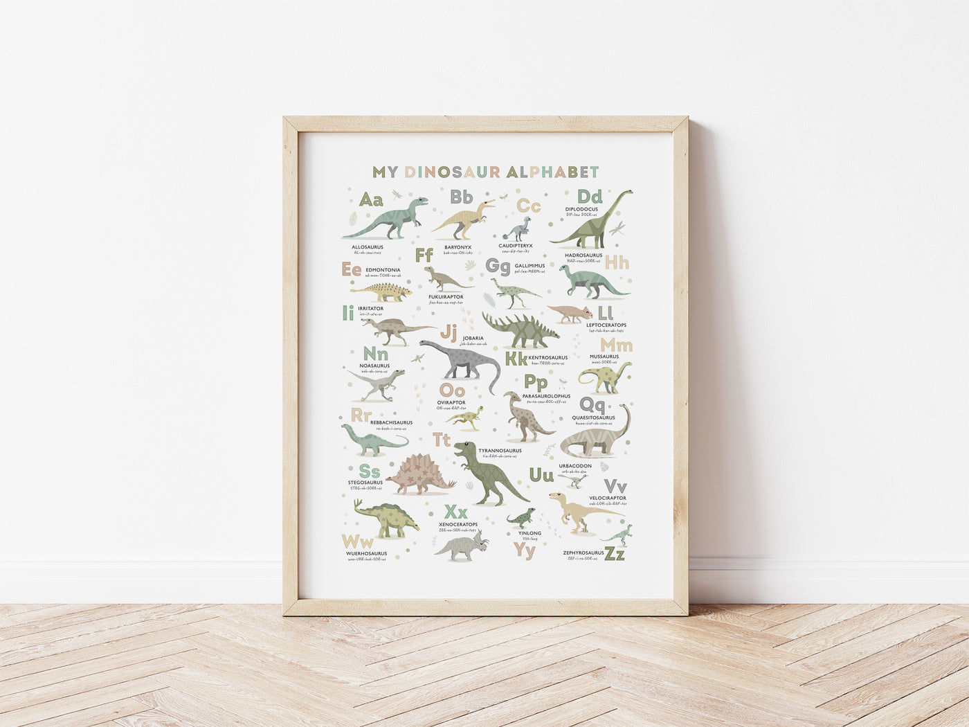 Dinosaur Alphabet Poster in Earth Tone Colours framed in oak, leaning against a white wall on a wooden floor
