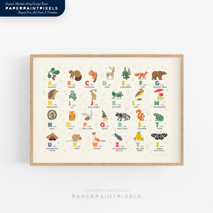 A horizontal, landscape printable of the Woodland Alphabet, shown framed above a crib in a calm, nature-themed nursery